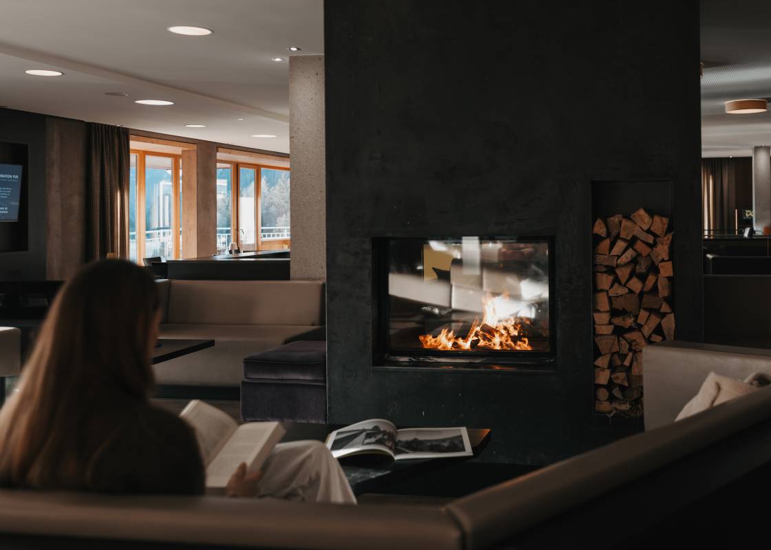 Frau sitzt in der Lounge vor dem Kamin und liest ein Buch