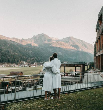 Paar steht im Bademantel auf einer Wiese und blickt auf die Alpen